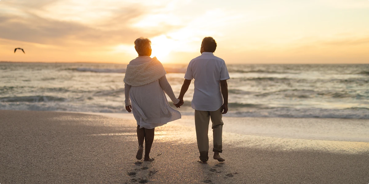 Senior couple holding hands while walking on the beach at sunset
